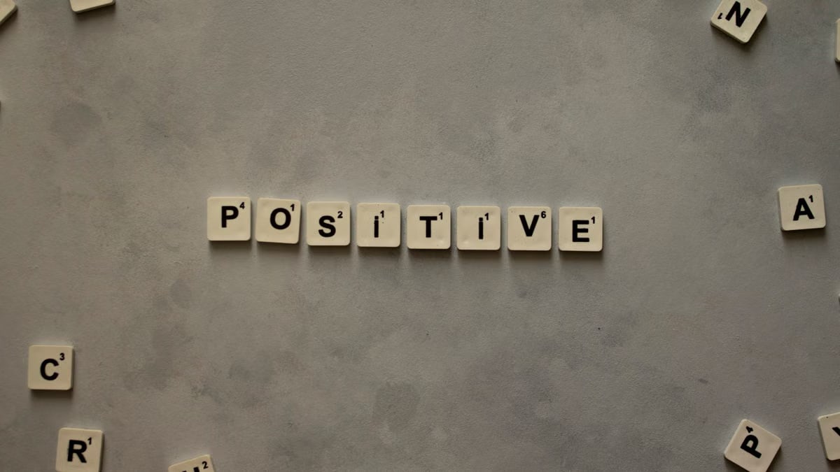 Scrabble tiles arranged to spell 'positive' on a gray textured surface, conveying optimism.